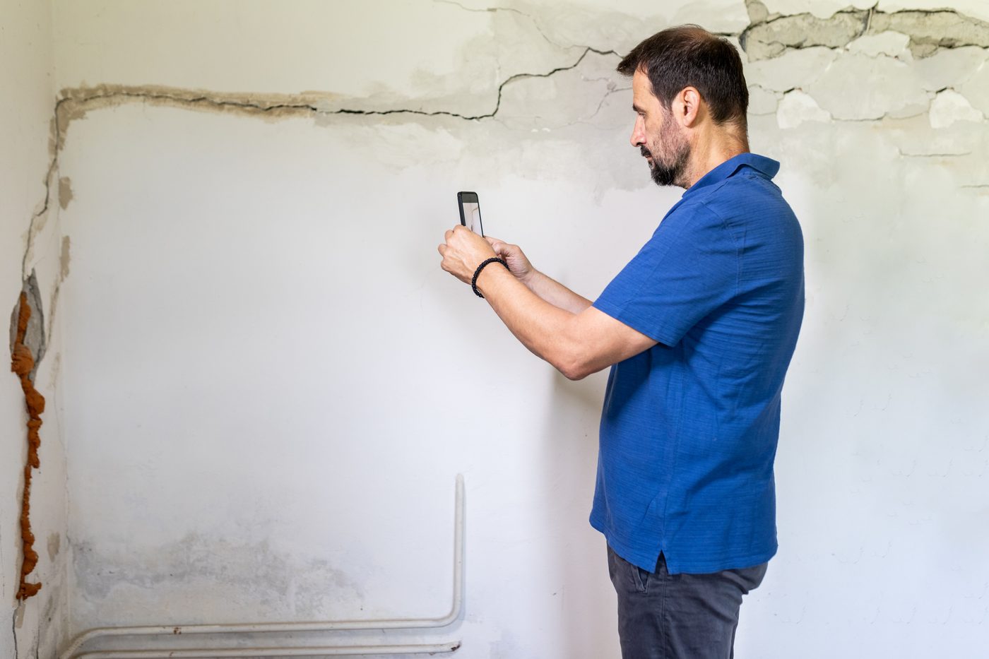 Homeowner photographing a plaster crack to document it for a structural engineer