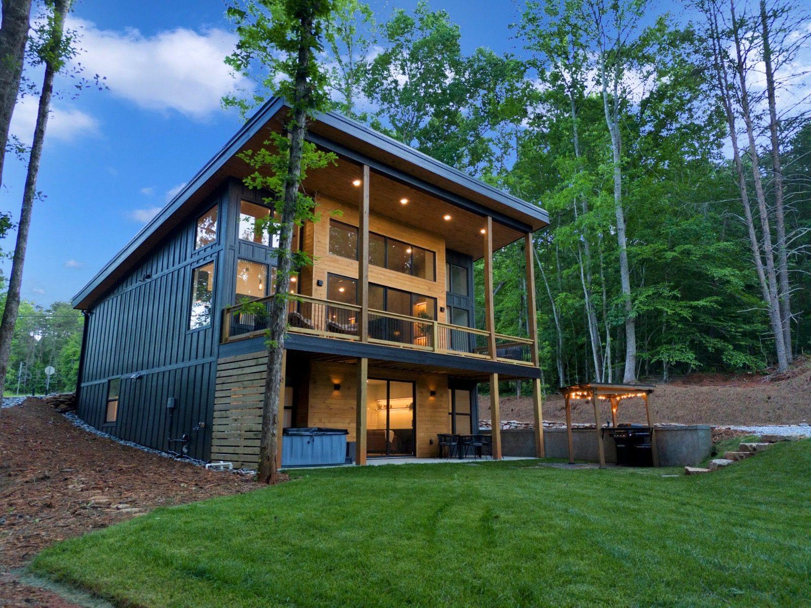 A completed modern two-story home in the woods at dusk, with a covered porch and exposed post-and-beam framing