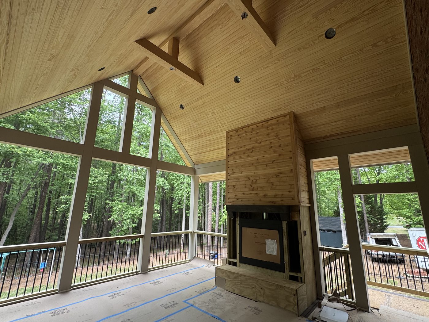 A client's screened-porch addition under construction — vaulted tongue-and-groove ceiling, exposed beams, and an outdoor fireplace tied into the existing home